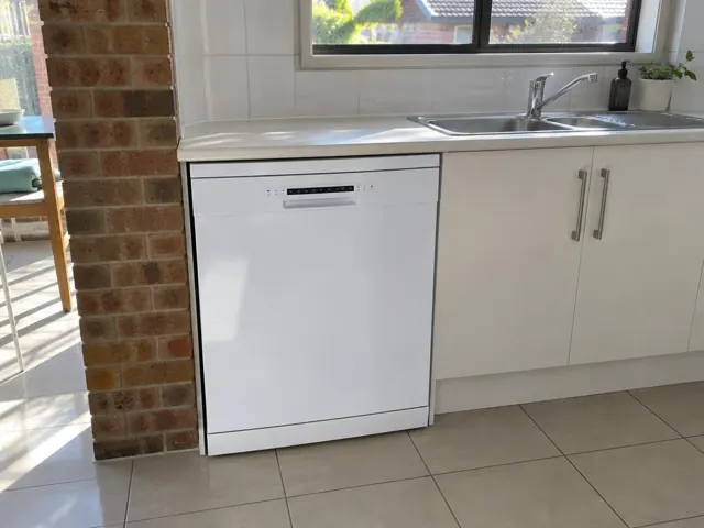 White dishwasher fitted under a kitchen benchtop beside a sink and brick wall in Cooks Hill