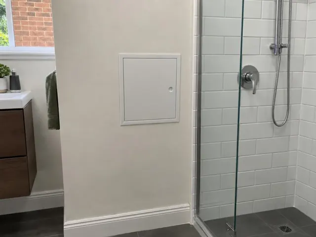 Neat access panel on a painted bathroom wall beside a tiled shower in The Hill