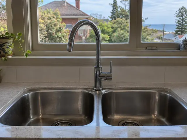 Chrome kitchen mixer tap above a double stainless sink with tiled splashback and window in Bar Beach