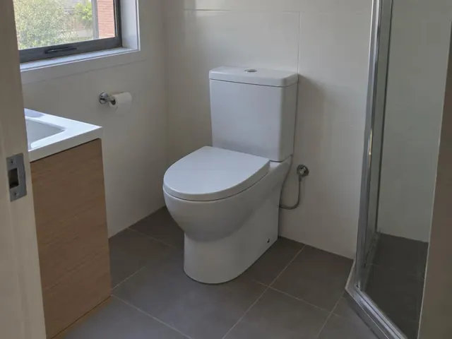 White toilet in a tiled bathroom beside a shower screen and vanity in Newcastle